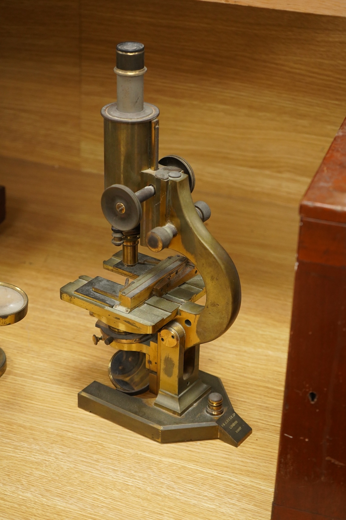 An early 20th century brass compound monocular microscope, by R & J Beck, Ltd., London, number 33007, with accessories including spare lenses, a free standing magnifier and objectives, mahogany cased; 34.5cm high, 19cm w